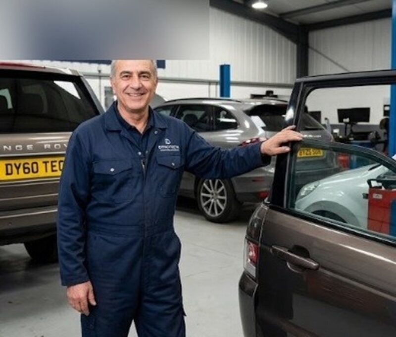 A technician beside a car in a busy workshop